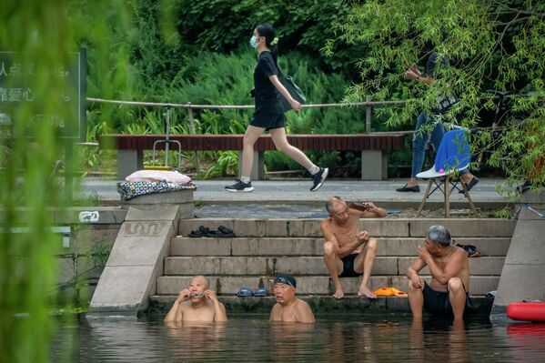 Một phụ nữ đeo khẩu trang đi ngang qua những người đàn ông đang tắm trong ngày nắng nóng ở Bắc Kinh. - Sputnik Việt Nam