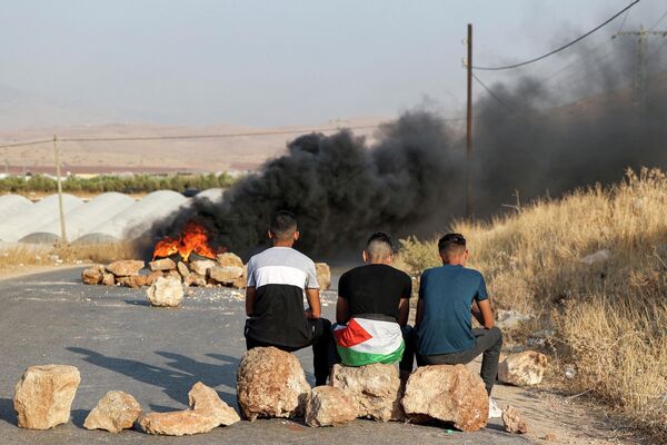 Người đàn ông Palestine ngồi trên những tảng đá gần lốp xe đang cháy để phản đối việc đóng đường gần địa điểm xảy ra vụ tấn công một chiếc xe buýt của Israel ở phía đông thành phố Tubas của Palestine. - Sputnik Việt Nam
