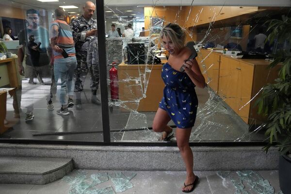 Nhân viên ngân hàng rời khỏi nhà băng qua ô cửa sổ bị những kẻ tấn công đập vỡ ở Beirut, Lebanon. - Sputnik Việt Nam