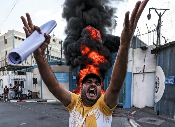 Người biểu tình Palestine giương biểu ngữ bên chỗ đốt cháy lốp xe ở thành phố Gaza. - Sputnik Việt Nam