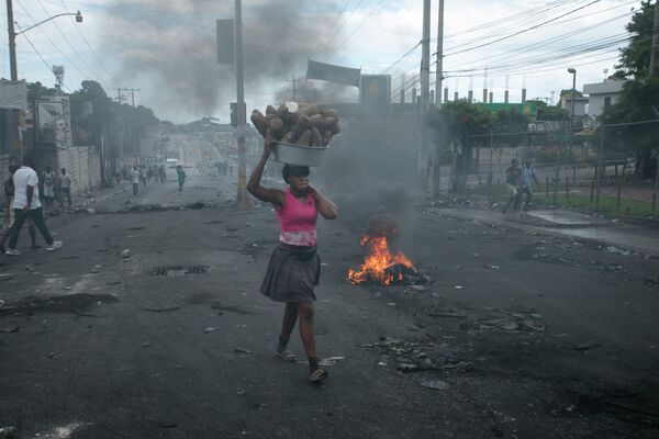 Người bán hàng rong đi qua hàng rào chắn do đám biểu tình dựng lên để phản đối tăng giá nhiên liệu và đòi Thủ tướng Haiti Ariel Henry từ chức ở Port-au-Prince, Haiti. - Sputnik Việt Nam