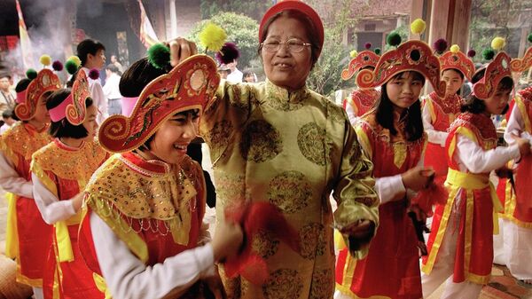 Женщина кладет фальшивые деньги в качестве подношения в шляпу молодой танцовщицы в пагоде во время начала 3-дневного празднования весеннего фестиваля в деревне Чу Донг Ту на севере Вьетнама - Sputnik Việt Nam