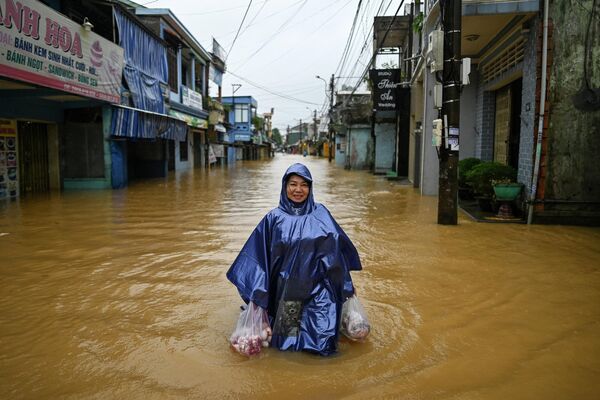 Người phụ nữ bán hàng tạp hóa băng qua dòng nước lũ xuống một con phố ở thành phố Huế, miền Trung Việt Nam. - Sputnik Việt Nam
