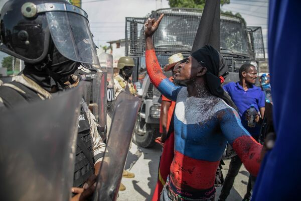 Một người biểu tình vẽ trên người màu lá quốc kỳ Nga tranh cãi với cảnh sát trước đại sứ quán Mỹ trong cuộc biểu tình ở Port-au-Prince, Haiti. - Sputnik Việt Nam
