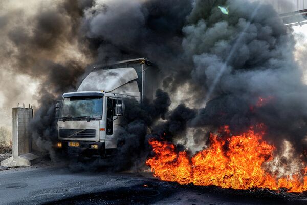 Xe tải hướng đến những chiếc xe đẩy qua các lốp xe đang cháy ở trạm kiểm soát Hawara. - Sputnik Việt Nam