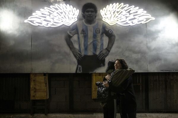 Phụ nữ ôm nhau khi gặp gỡ bên bức ảnh của Diego Maradona ở Buenos Aires. - Sputnik Việt Nam