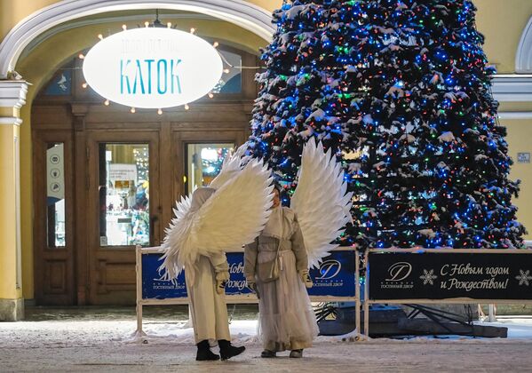 Những người biểu diễn đường phố ăn mặc như những thiên thần bên ngoài Gostiny Dvor ở St. Petersburg, được trang trí cho Năm Mới. - Sputnik Việt Nam
