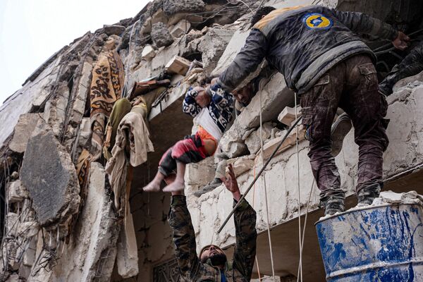 Người dân đưa đứa trẻ ra khỏi đống đổ nát trong tòa nhà bị sập sau trận động đất ở thành phố Jandaris, tây bắc Syria. - Sputnik Việt Nam