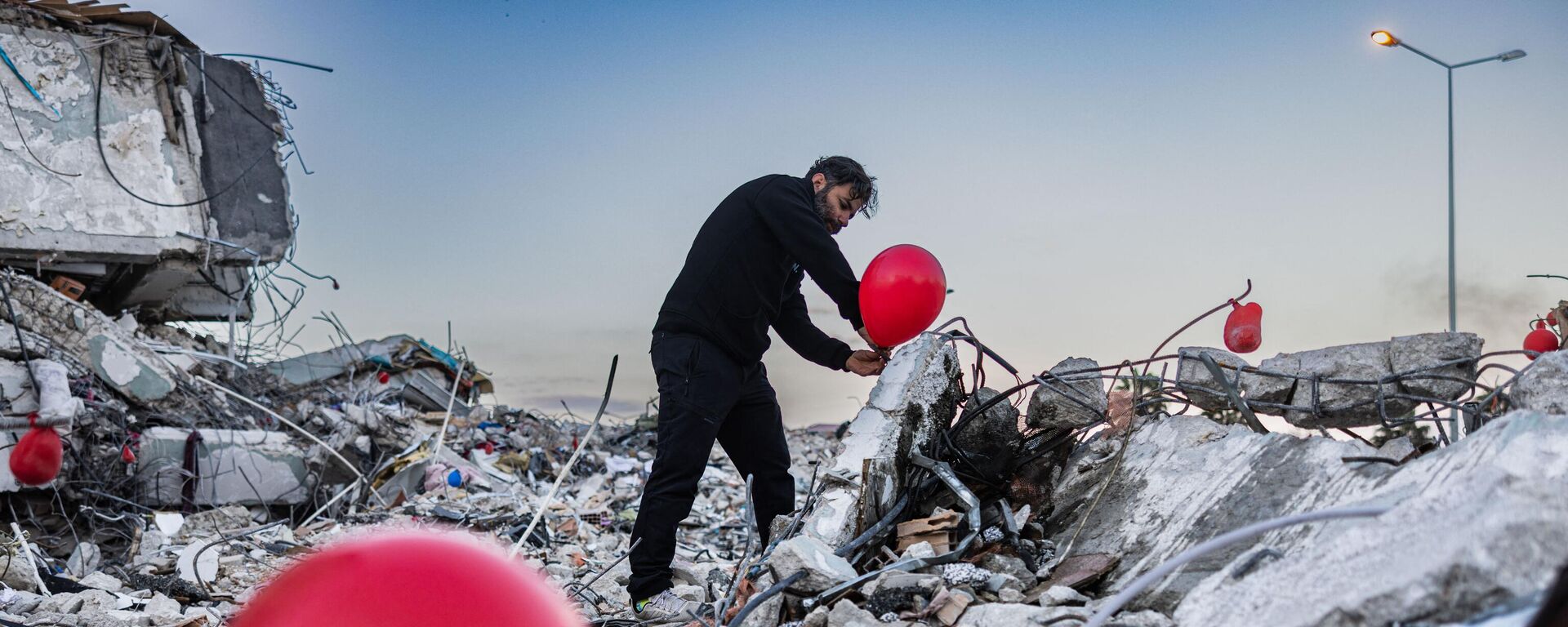 Ogun Sever Our, 38 tuổi, treo quả bóng bay trên đống đổ nát tòa nhà bị sập ở Antakya, miền nam Thổ Nhĩ Kỳ. - Sputnik Việt Nam, 1920, 23.02.2023