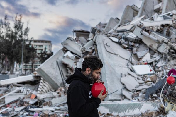 Ogun Sever Okur, 38 tuổi, thổi phồng quả bóng bay để treo trên đống đổ nát tòa nhà bị sập ở Antakya, miền nam Thổ Nhĩ Kỳ. - Sputnik Việt Nam