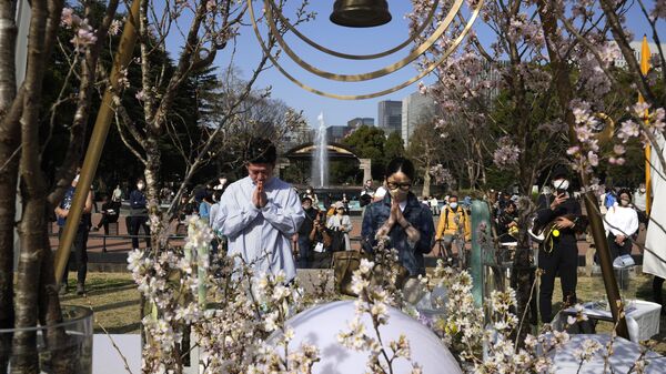 Một người đàn ông và một người phụ nữ cầu nguyện sau khi đặt hoa trước đài tưởng niệm được dựng lên để kỷ niệm 12 năm thảm họa động đất, sóng thần và hạt nhân lớn ở Công viên Hibiya ở Tokyo - Sputnik Việt Nam