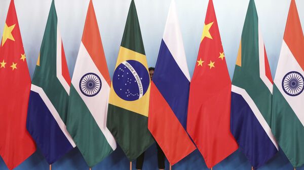 Staff worker stands behinds national flags of Brazil, Russia, China, South Africa and India to tidy the flags ahead of a group photo during the BRICS Summit at the Xiamen International Conference and Exhibition Center in Xiamen, southeastern China's Fujian Province, Monday, Sept. 4, 2017. - Sputnik Việt Nam