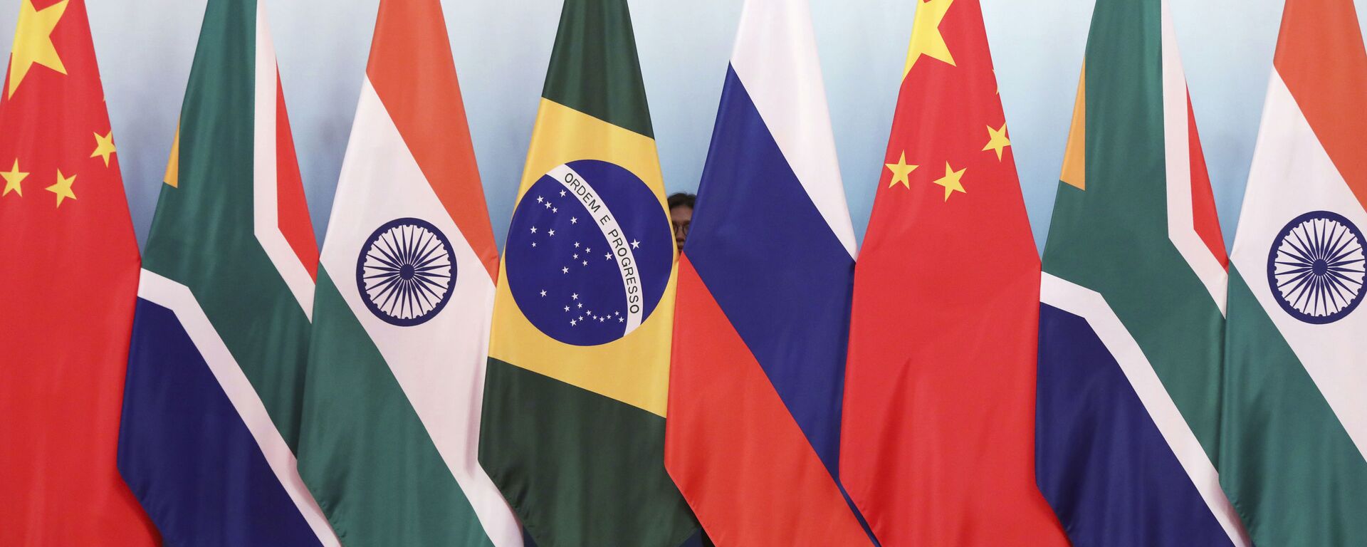 Staff worker stands behinds national flags of Brazil, Russia, China, South Africa and India to tidy the flags ahead of a group photo during the BRICS Summit at the Xiamen International Conference and Exhibition Center in Xiamen, southeastern China's Fujian Province, Monday, Sept. 4, 2017. - Sputnik Việt Nam, 1920, 10.06.2023