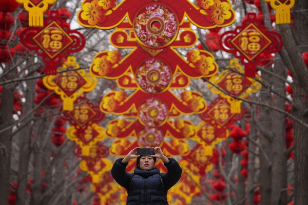Một người phụ nữ chụp ảnh bằng điện thoại thông minh những chiếc đèn lồng đỏ và đồ trang trí bằng cây trước Tết Nguyên đán ở Công viên Ditan, Bắc Kinh. - Sputnik Việt Nam