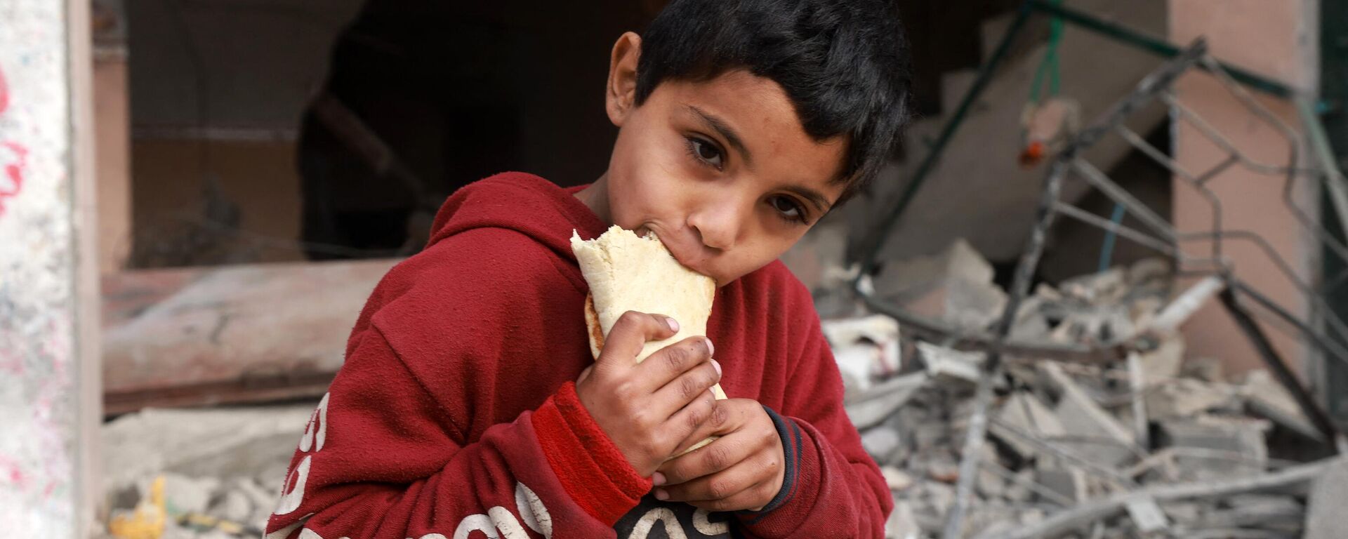 Một đứa trẻ ăn trước một tòa nhà bị hư hại trong vụ đánh bom của Israel ở Rafah - Sputnik Việt Nam, 1920, 06.03.2024