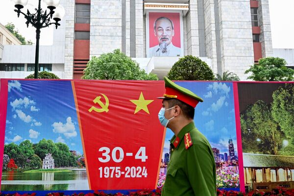 Một sĩ quan cảnh sát đi ngang qua bảng quảng cáo trước Ngày thống nhất đất nước Việt Nam, 30 tháng 4 tại Hà Nội, Việt Nam - Sputnik Việt Nam