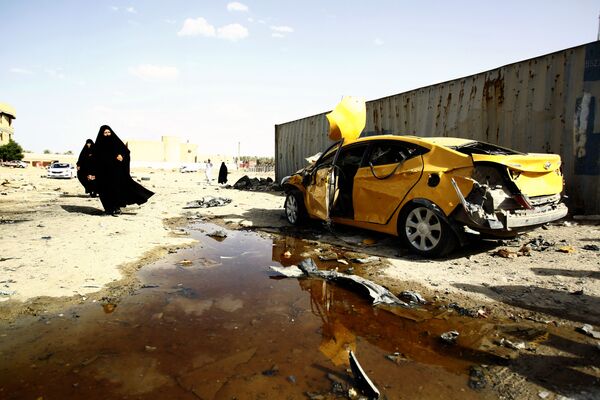 Người phụ nữ đi bộ qua  chiếc xe bị hỏng nặng, kết quả của các cuộc tấn công khủng bố, Iraq - Sputnik Việt Nam