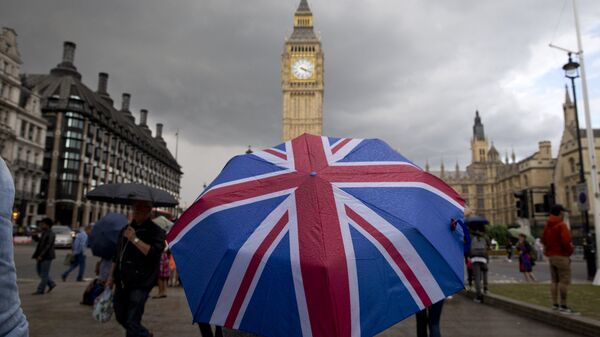 A pedestrian shelters from the rain beneath a Union flag themed umbrella as they walk near the Big Ben clock face and the Elizabeth Tower at the Houses of Parliament in central London on June 25, 2016. - Sputnik Việt Nam