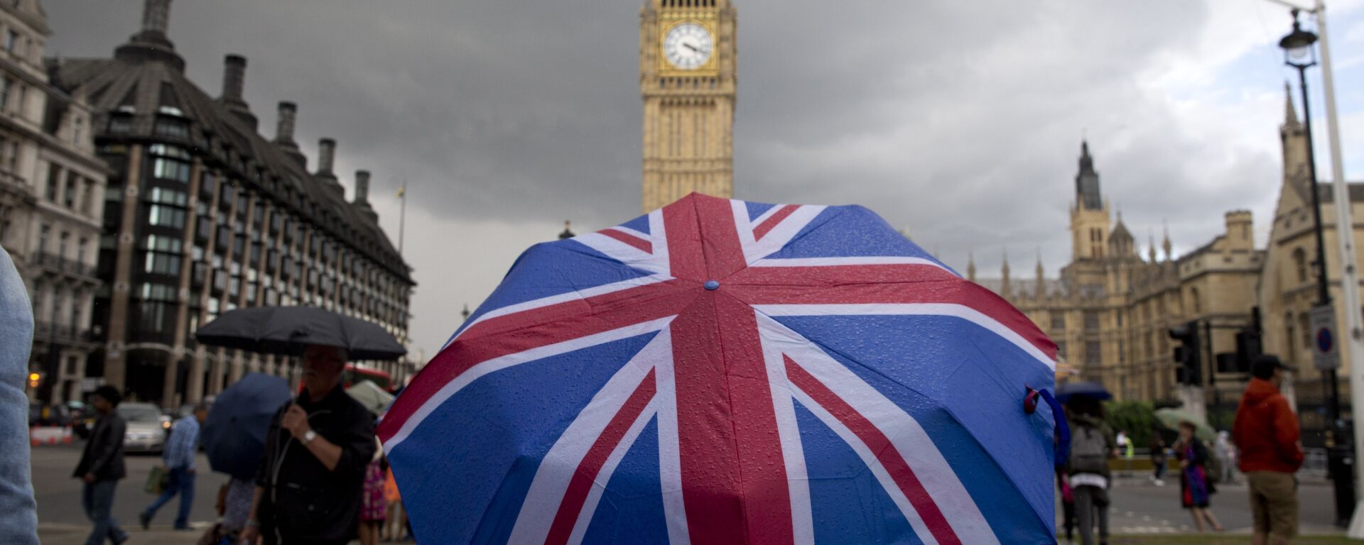 A pedestrian shelters from the rain beneath a Union flag themed umbrella as they walk near the Big Ben clock face and the Elizabeth Tower at the Houses of Parliament in central London on June 25, 2016. - Sputnik Việt Nam, 1920, 20.08.2022