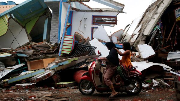 A woman and child ride a motorcycle past damaged buildings following this week's strong earthquake in Meureudu market, Pidie Jaya, Aceh province, Indonesia December 9, 2016. - Sputnik Việt Nam