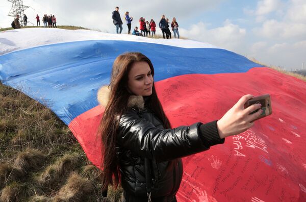 Nga, Cộng hòa Crưm. Cô gái chụp ảnh “tự sướng” trên nền lá cờ Nga khổng lồ tại lễ hội Mùa xuân Crưm”. - Sputnik Việt Nam