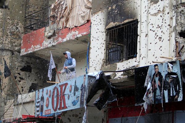 Người đàn ông trên ban-con tòa nhà ghi dấu vết của trận oanh kích trong trại tị nạn gần thành phố Saida (Lebanon). - Sputnik Việt Nam