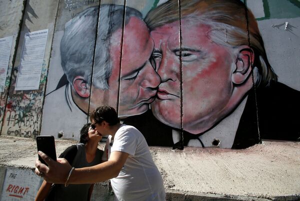 Du khách chụp ảnh trên nền tranh phun sơn graffiti mô tả nụ hôn của Thủ tướng Israel Binyamin Netanyahu và Tổng thống Hoa Kỳ Donald Trump trên bức tường Bethlehem, Palestine - Sputnik Việt Nam