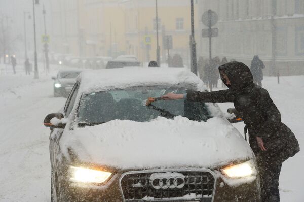 Chủ sở hữu đang dọn tuyết bám trên chiếc xe hơi của mình trong cơn tuyết đổ xuống - Sputnik Việt Nam
