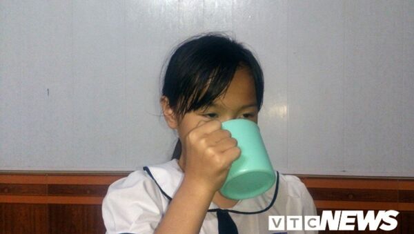 Bé Phương Anh cầm cái cốc ở nhà mô tả lại cái cốc tương tự em đã từng uống 1/2 nước giặt giẻ lau bảng ở lớp do cô giáo phạt. - Sputnik Việt Nam