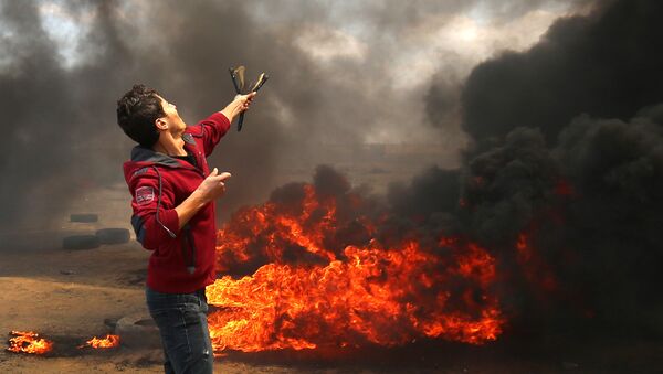A Palestinian man uses a slingshot during clashes with Israeli forces along the border with the Gaza strip east of Khan Yunis on May 14, 2018, as Palestinians protest over the inauguration of the US embassy following its controversial move to Jerusalem - Sputnik Việt Nam