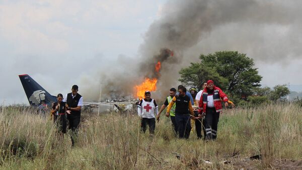 In this photo released by Red Cross Durango communications office, Red Cross workers and rescue workers carry an injured person on a stretcher, right, as airline workers, left, walk away from the site where an Aeromexico airliner crashed in a field near the airport in Durango, Mexico, Tuesday, July 31, 2018 - Sputnik Việt Nam