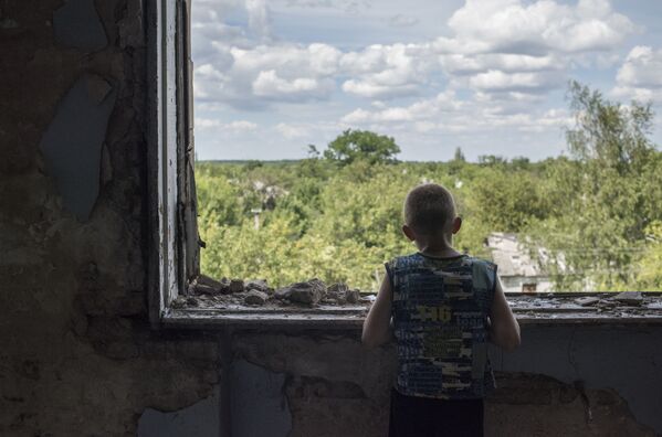 Một thiếu niên ngồi bên cửa sổ phòng thể thao đổ nát của trường trung học làng Shakhty 6/7, nơi cư dân địa phương Gorlovka, Cộng hòa Nhân dân tự xưng Donetsk đến trú ẩn - Sputnik Việt Nam