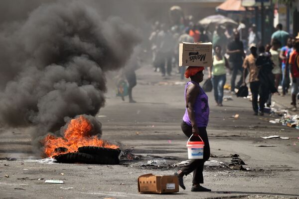Người phụ nữ đi ngang chiếc lốp xe đang cháy trên đường phố Port-au-Prince, thủ đô Haiti - Sputnik Việt Nam