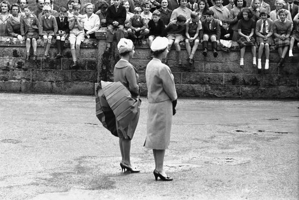 Gió nâng váy của Công chúa Margaret khi cô và Nữ hoàng Elizabeth II chờ Tổng thống Mỹ Dwight Eisenhower xuất hiện tại Lâu đài Balmoral, Scotland, 1959 - Sputnik Việt Nam