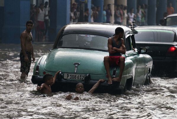 Các thanh niên trên thanh cản sau của một chiếc xe Mỹ cũ trên một phố bị ngập lụt ở Havana, Cuba - Sputnik Việt Nam