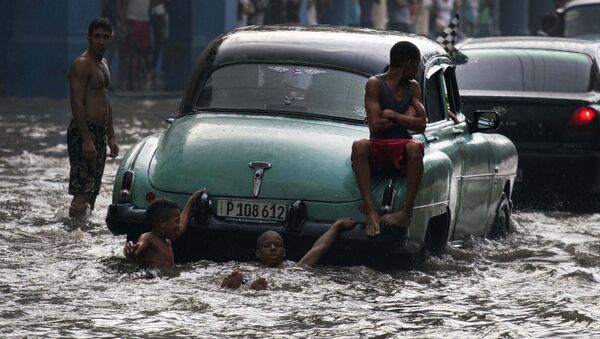 Các thanh niên trên thanh cản sau của một chiếc xe Mỹ cũ trên một phố bị ngập lụt ở Havana, Cuba - Sputnik Việt Nam