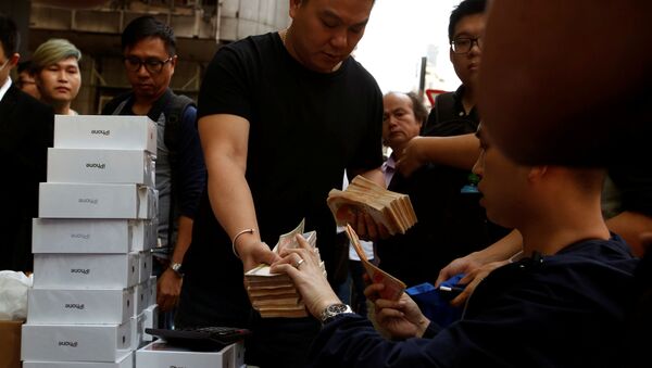 Một người đàn ông cầm một đống tiền giấy để mua một chiếc iPhone X mới mà những người vừa mua nó tại một cửa hàng Apple đang bán lại nó trên một con phố ở Hồng Kông, Trung Quốc. - Sputnik Việt Nam