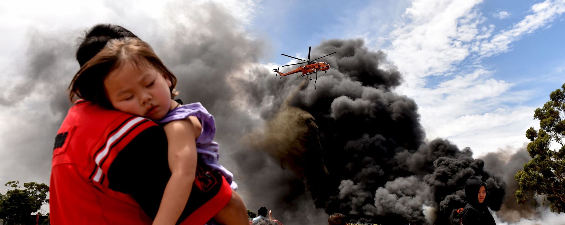 Người dân địa phương nhìn vào một chiếc trực thăng hạ xuống bên cạnh khói lớn từ đám cháy ở Melbourne - Sputnik Việt Nam, 1920, 18.02.2020