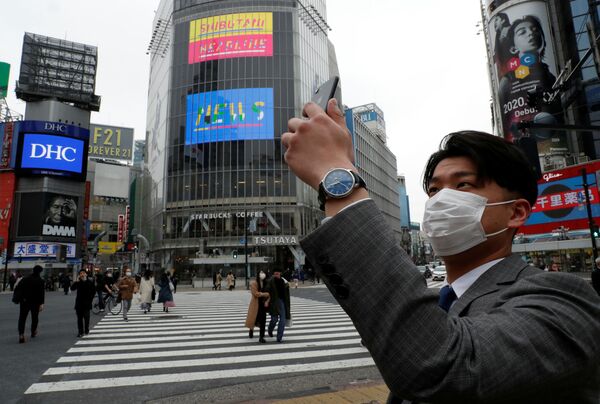 Một người đàn ông đeo khẩu trang chụp ảnh trên điện thoại di động vào buổi trưa tại ngã tư Shibuya ở Tokyo trong đại dịch coronavirus - Sputnik Việt Nam