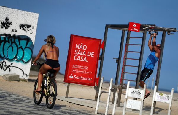 Cô gái đi xe đạp ngang qua tấm áp phích Đừng ra khỏi nhà trên Bãi biển Ipanema ở Rio de Janeiro, Brazil - Sputnik Việt Nam