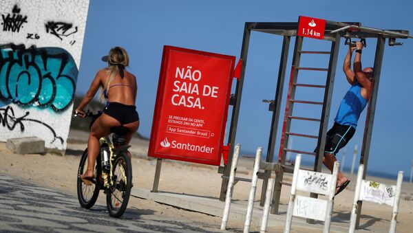 Cô gái đi xe đạp ngang qua tấm áp phích Đừng ra khỏi nhà trên Bãi biển Ipanema ở Rio de Janeiro, Brazil - Sputnik Việt Nam