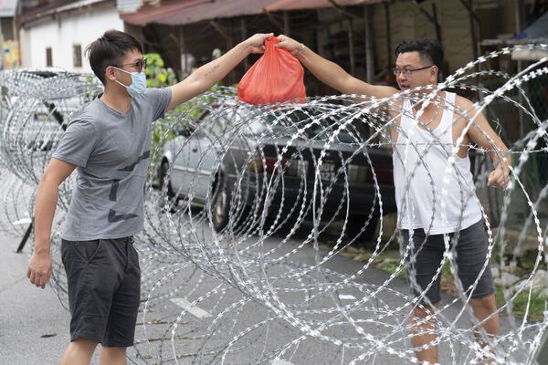 Người đàn ông chuyển cái túi qua hàng rào thép gai ở khu vực Kuala Lumpur, Malaysia - Sputnik Việt Nam