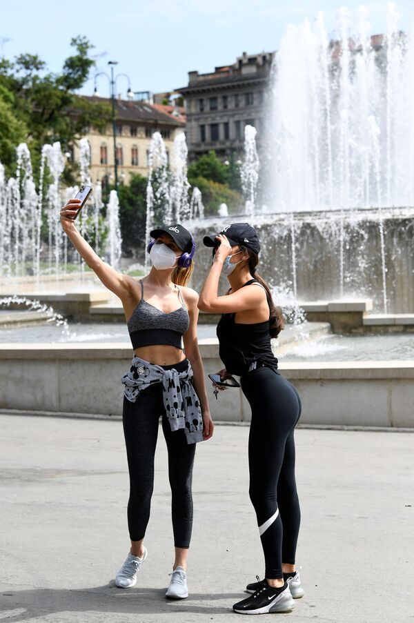 Các cô gái đeo khẩu trang y tế chụp ảnh tự sướng với đài phun nước ở Quảng trường Castell ở Milan - Sputnik Việt Nam