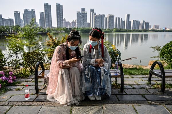 Phụ nữ trẻ đeo khẩu trang và bận trang phục truyền thống trên băng ghế ở công viên Vũ Hán, Trung Quốc - Sputnik Việt Nam