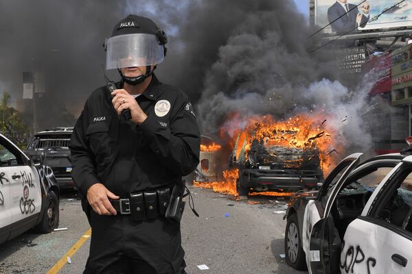 Cảnh sát Los Angeles trên nền chiếc xe bị đốt cháy trong cuộc biểu tình - Sputnik Việt Nam