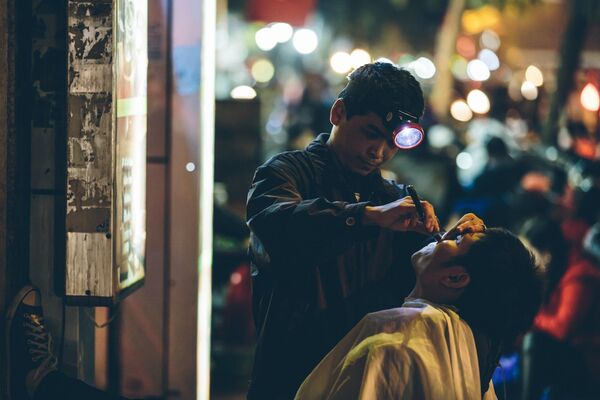 Người thợ cát tóc cho khách hàng dưới ánh đèn đường ở Hà Nội, Việt Nam - Sputnik Việt Nam